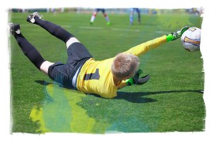 Kids soccer goalkeeper catching a low ball on the ground