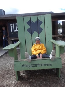 Carol sitting in a large green chair with an X and #flagstaffextreme