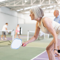 An older woman playing pickleball on an inside court.
