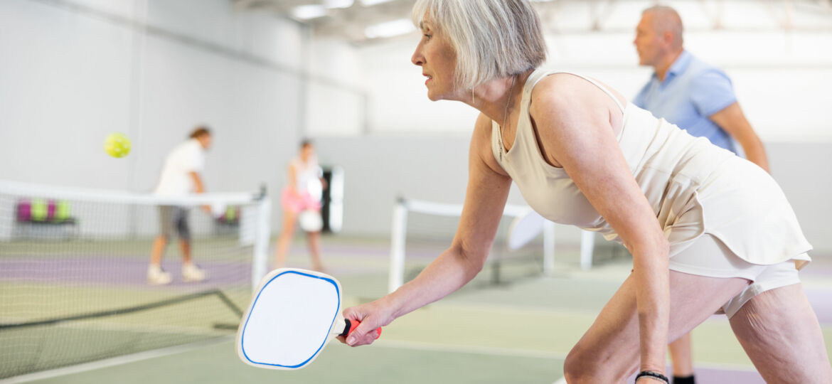 An older woman playing pickleball on an inside court.