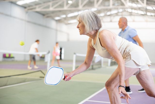 An older woman playing pickleball on an inside court.